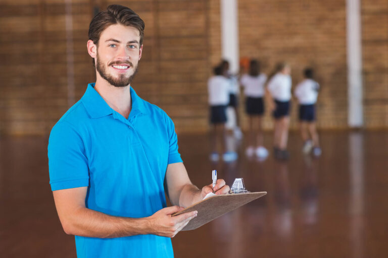 Portrait,Of,Sports,Teacher,Writing,On,Clipboard,In,Basketball,Court