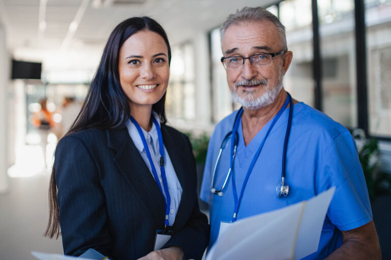 Portrait,Of,Elderly,Doctor,And,Business,Woman,At,Hospital,Corridor.