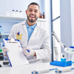 Hispanic,Man,Working,At,Scientist,Laboratory,Holding,Blank,Clipboard,Smiling