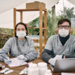 Two,Gloved,Clinician,In,Uniform,Working,By,Table,In,Large